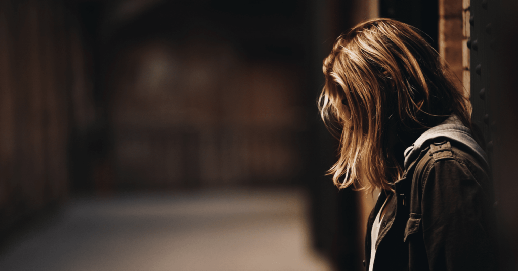 A side profile photo of a woman with brown hair standing in an alley 